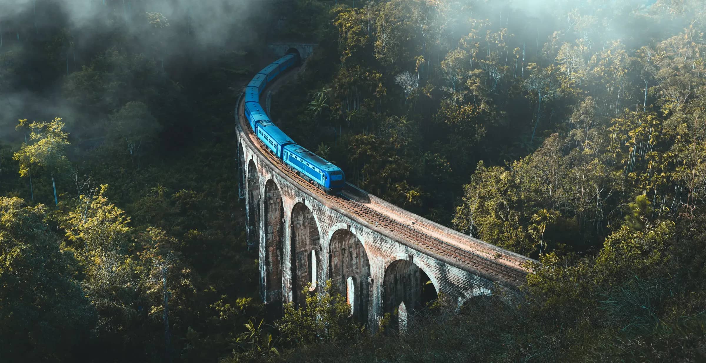 Blue train crossing the Nine Arches Bridge near Ella in the mist